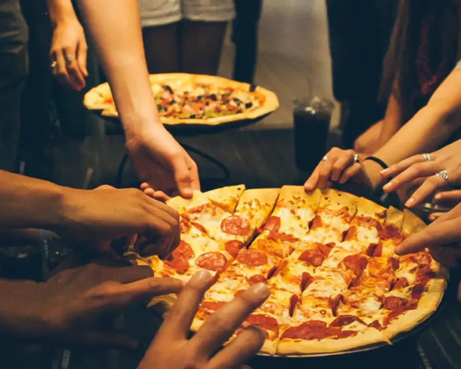 Friends sharing pizza slices at Pro Bowl West in Fort Wayne, IN